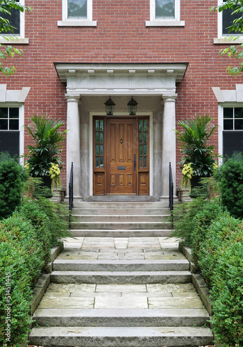 Long flagstone path leading to portico entrance of traditional brick house, with elegant wood grain front door with sidelights