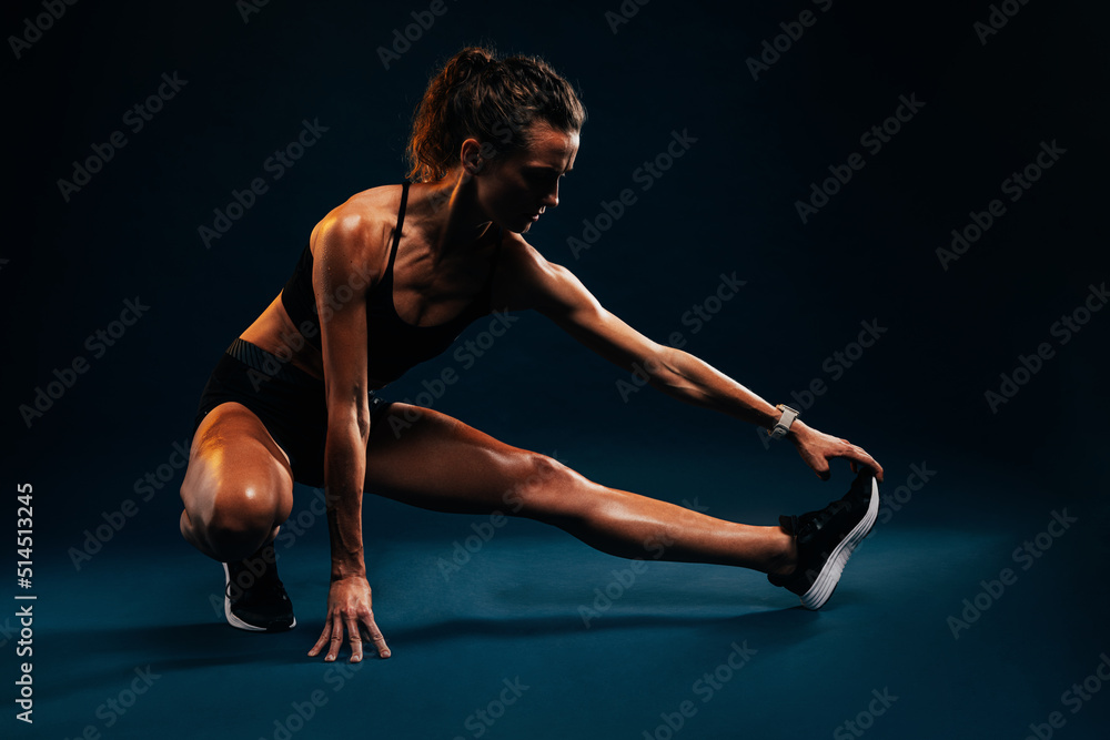 Muscular woman stretching her leg on black background