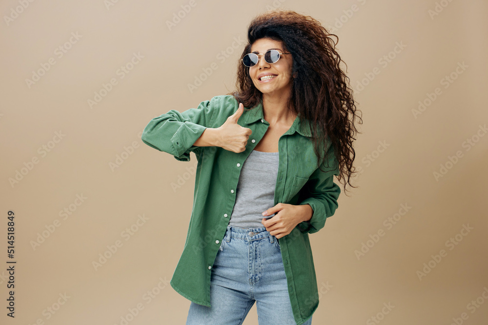 PEACE CONCEPT. Smiling friendly tanned curly Latin female in casual things sunglasses gesture thumb up posing isolated over pastel beige background. Copy space Mockup Banner. Fashion offer