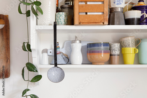 Vintage style kitchen wooden shelf with kitchen utensils. Storage open cupboard, ceramic crockery stand on a shelf in the kitchen. Set of colourful dishes in modern interior, home decor. photo