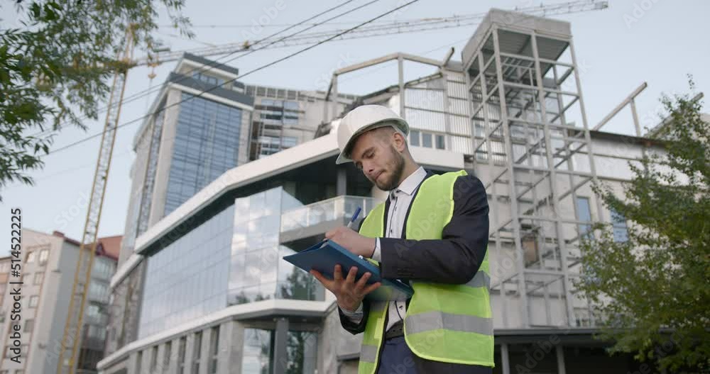 Male architect in helmet writing in notepad at building site Male architect in helmet writing in notepad at building site