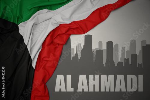 abstract silhouette of the city with text Al Ahmadi near waving national flag of kuwait on a gray background. photo