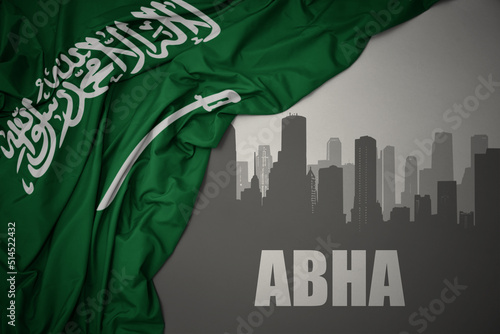 abstract silhouette of the city with text Abha near waving national flag of saudi arabia on a gray background. photo