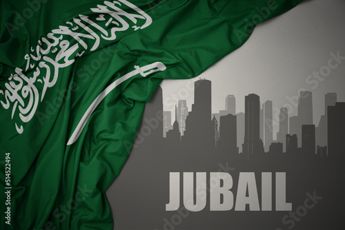 abstract silhouette of the city with text Jubail near waving national flag of saudi arabia on a gray background. photo