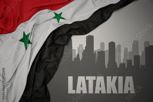 abstract silhouette of the city with text Latakia near waving national flag of syria on a gray background. photo