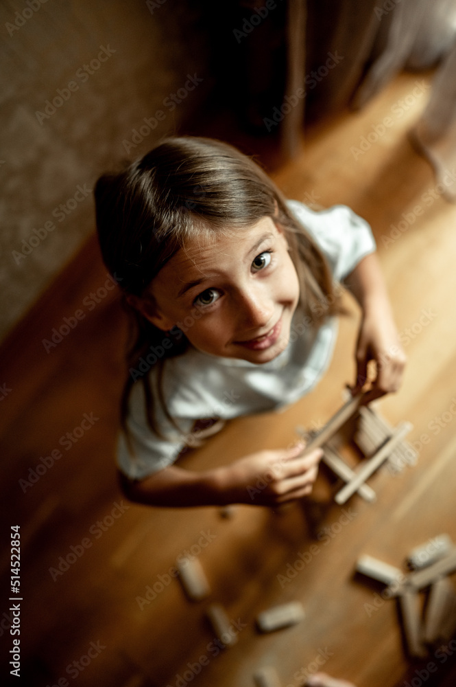 a girl of 5-6 years old plays in the room in indushki, a child builds a tower of wooden sticks, a girl plays a construction set, educational toys for home and kindergarten