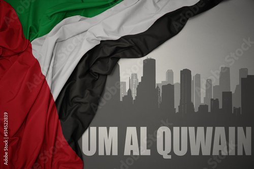 abstract silhouette of the city with text Um al quwain near waving national flag of united arab emirates on a gray background. photo