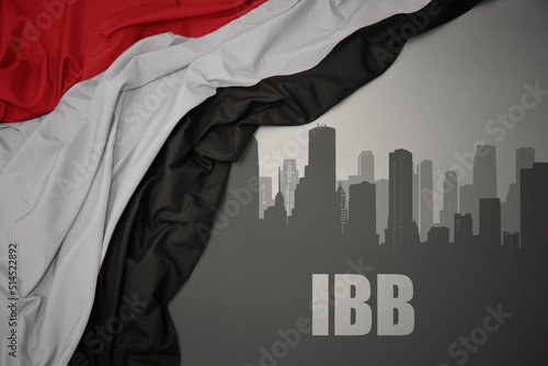 abstract silhouette of the city with text Ibb near waving national flag of yemen on a gray background. photo