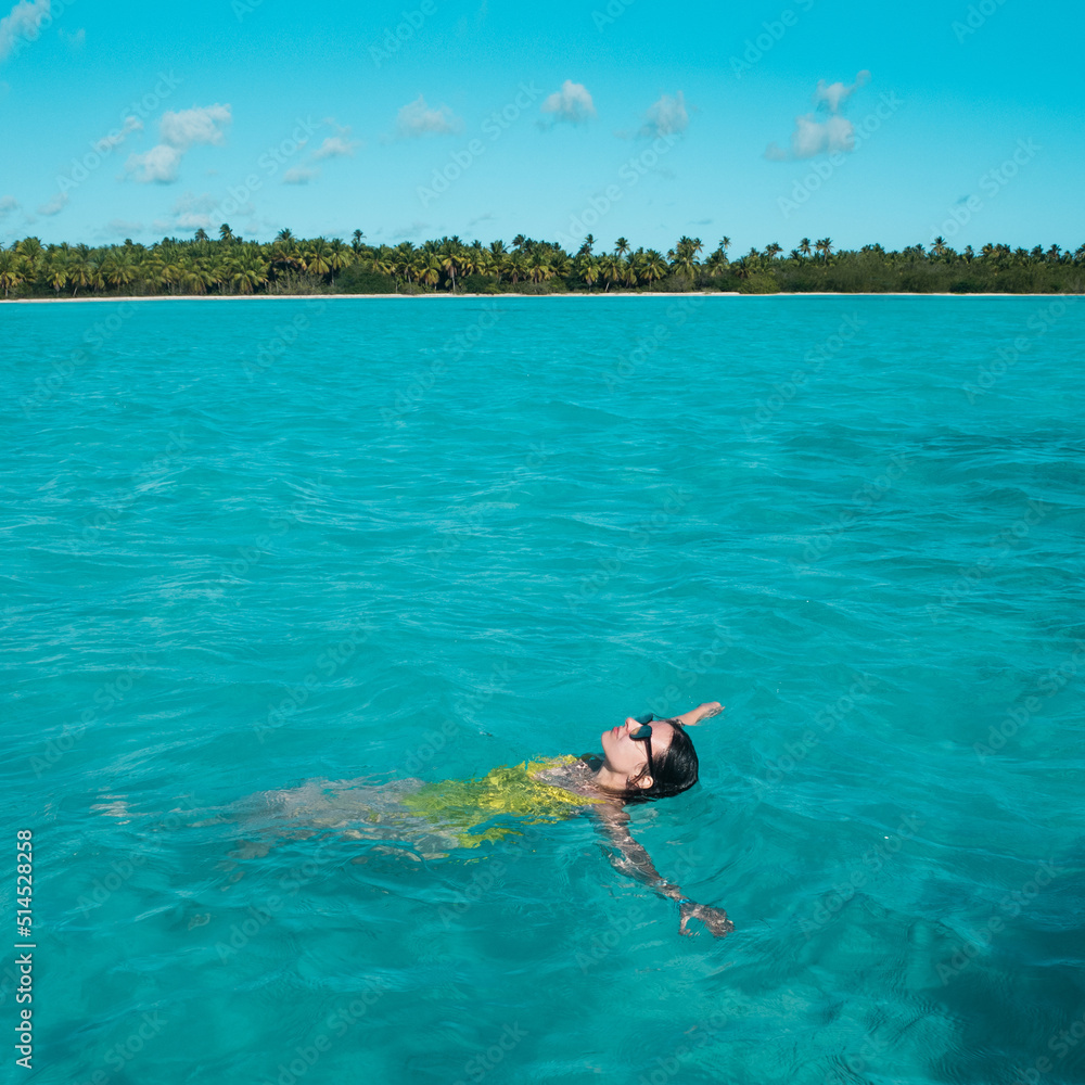 young woman in a one-piece yellow swimsuit floats on the surface of the water. Brunette girl relaxes and bathes in the blue sea, relaxing by the sea