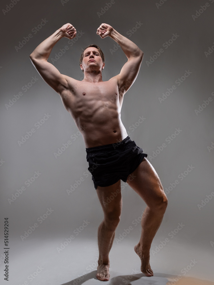 Muscular man in an artistic pose, portrait on a gray background. The guy is an athlete in a wrestling pose. A muscular bodybuilder strains his fists