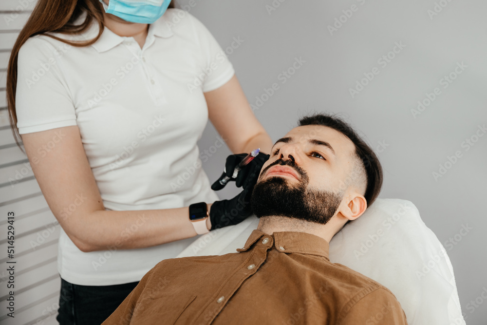 Fototapeta premium Beauty treatments for a stylish young man with a beard. Beautician makes beauty injections in a man's face