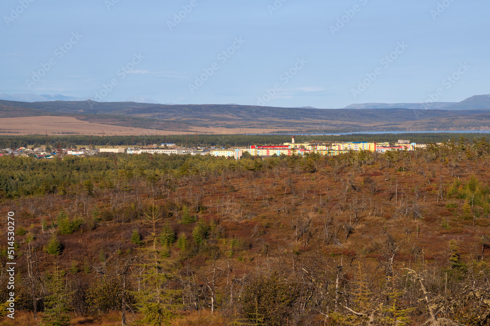 View of the northern town and forest-tundra. Colored buildings in the distance. Nature and settlements of Siberia. Surroundings of the urban-type settlement of Ola. Magadan region, Far East of Russia.
