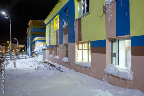 Night winter view of a residential building and a snow-covered street in a northern city in the Arctic. Multi-colored buildings among the snow. Anadyr, Chukotka, Far North of Russia. The polar region. © Andrei Stepanov