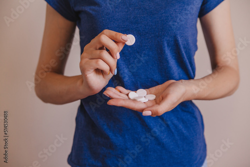 Close-up of an unrecognizable woman holding pills in her hand. The patient holds the medicines in his hand. Background of a girl in a blue t-shirt is holding medicines.