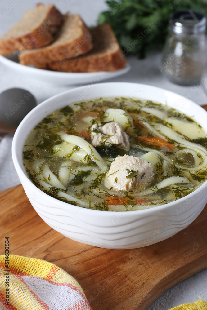 Soup with turkey, noodles and vegetables in white bowl on wooden board