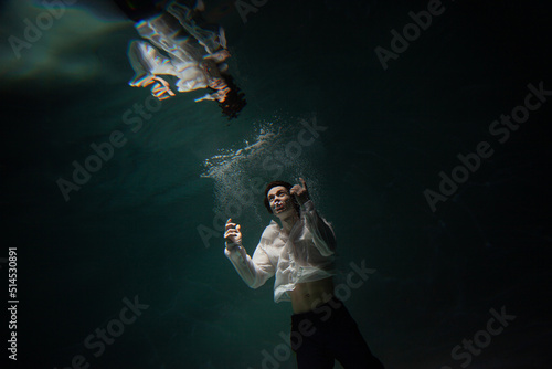 underwater shooting with contrasting light, a guy in a white shirt and pants screaming underwater, panicking and afraid of drowning, falling into the water, a crime.