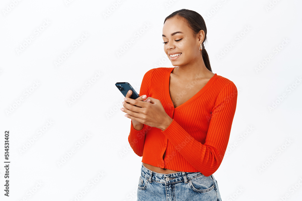 Smiling modern woman using mobile phone, chatting in app, standing in red blouse over white background Smiling modern woman using mobile phone, chatting in app, standing in red blouse over white background