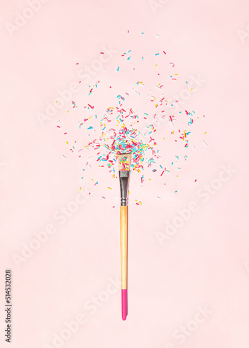 Creative sweets concept. Minimalistic composition with paint brush and sprinkles on light pink background. Tasty food idea. Coloring in sweet colors idea.