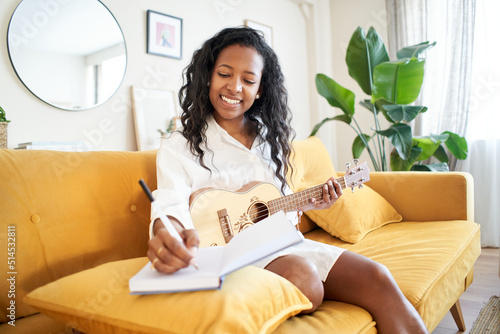 Woman singer-songwriter composing a song at home. Musical artist creating. Girl writing a song in a notebook sitting on the sofa. photo