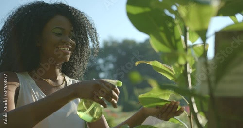 Pretty young afro-american girl with green eye shadows and neutral lipstick is beautifuly smiling and using the green plastic trigger spray for outdoor plants. photo