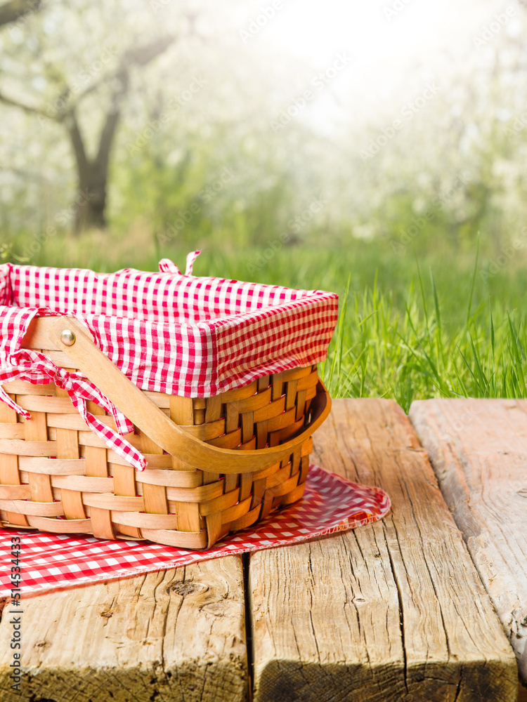 On a simple wooden table, a straw picnic basket against the backdrop of a  bright summer nature. Picnic, relaxation, delicious organic food, healthy  lifestyle. There is free space to insert. foto de