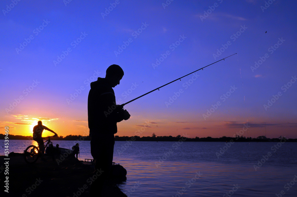 Silhouette of man fishing in Guaiba lake next to Gasometro at sunset time, in Porto Alegre, Rio Grande do Sul, Brazil Silhouette of man fishing in Guaiba lake next to Gasometro at sunset time, in Porto Alegre, Rio Grande do Sul, Brazil