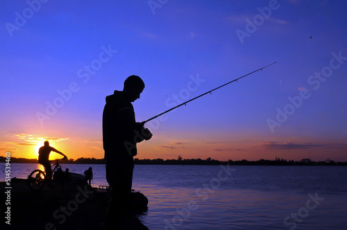 Silhouette of man fishing in Guaiba lake next to Gasometro at sunset time, in Porto Alegre, Rio Grande do Sul, Brazil