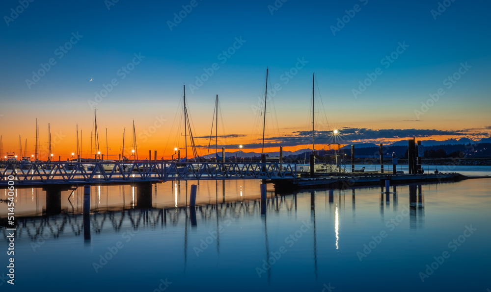 Beautiful sunset at the yacht harbor with pier. Summer sunset at the sea. Marina, port under dark blue sky at sunset