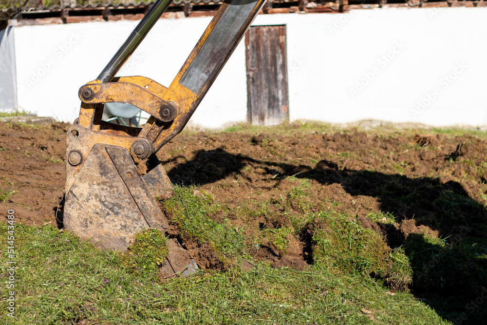 Fototapeta premium An bucket excavator in the village paves the way, digs soil and clears land.