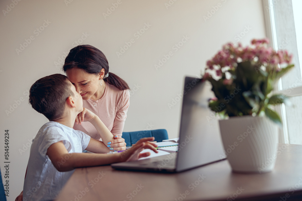Happy mother and small teen son cuddling nose to nose at home while learning online.