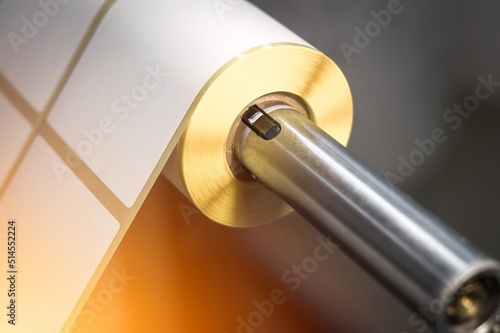 Roller of wound tape with self-adhesive white label on a cardboard spool mounted on the pneumatic shaft of the die-cutting machine for making a white label without printing. Selective focus