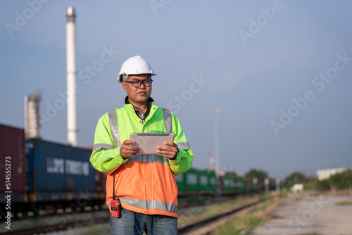 Engineer wearing uniform and helmet stand in front of the car hand holding blue print paper, inspection work plant site progress using radio communication to work orders with oil refinery background. photo