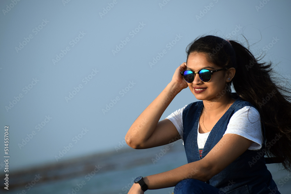 Pretty young lady enjoying the beauty of the blue sea. Beautiful woman sitting on the coral wearing black sun glass Pretty young lady enjoying the beauty of the blue sea. Beautiful woman sitting on the coral wearing black sun glass