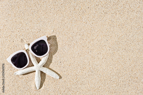 Starfish and white sunglasses on natural sand background, copy space, top view