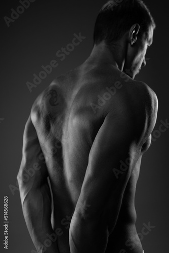 Fotografie a sporty, pumped-up handsome man poses on a dark background in a contoured light