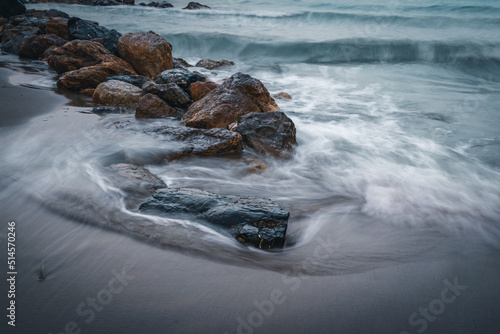 Beach on the Italian Riviera with sun, sea and stones in the sea water. Rough Sea and Foamy Waves on Shore at Mediterranean Coast in Sunrise