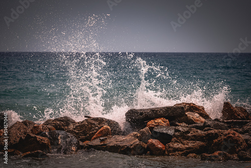 Beach on the Italian Riviera with sun, sea and stones in the sea water. Rough Sea and Foamy Waves on Shore at Mediterranean Coast in Sunrise
