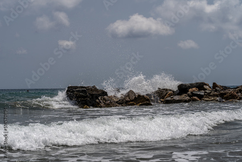 Beach on the Italian Riviera with sun, sea and stones in the sea water. Rough Sea and Foamy Waves on Shore at Mediterranean Coast in Sunrise