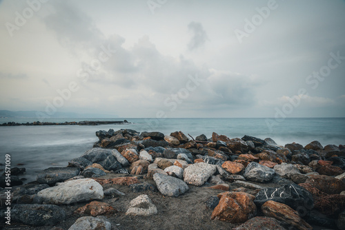 Beach on the Italian Riviera with sun, sea and stones in the sea water. Rough Sea and Foamy Waves on Shore at Mediterranean Coast in Sunrise