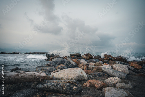 Beach on the Italian Riviera with sun, sea and stones in the sea water. Rough Sea and Foamy Waves on Shore at Mediterranean Coast in Sunrise