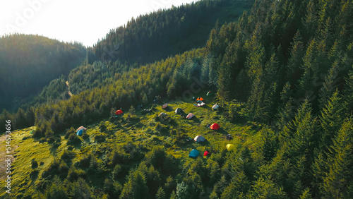 Camping tourists in the mountains. Dawn in the mountains. Tent camp of tourists in the mountains from a bird's eye view. Flight over the Christmas tree forest. Tents of tourists from a bird's eye view