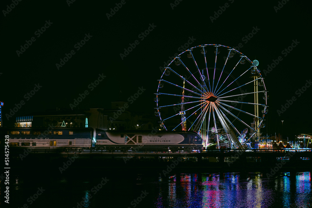 ferris wheel at night with train passing by.