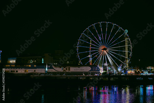 ferris wheel at night with train passing by.