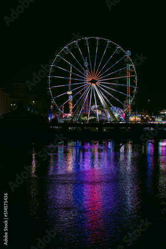 ferris wheel at night with reflection on water.