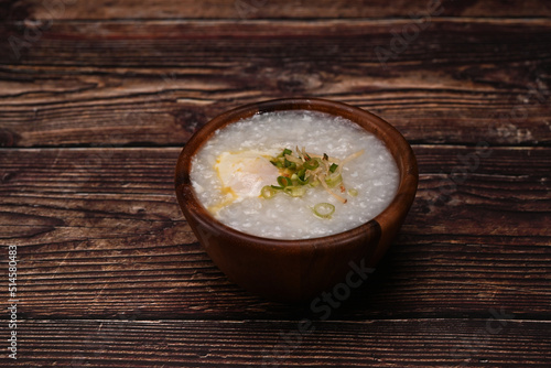 Rice porridge, rice gruel or congee with boiled egg ,sliced ginger and slice scallion in bowl on wooden table for light meal