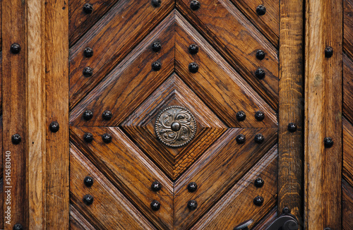Old wooden dark brown door with diamond-shaped pattern in the rays of daylight. Vintage background