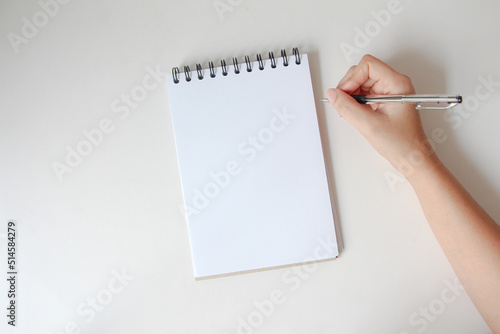 woman hand writing in empty notebook at the white desk. Flat lay top view.