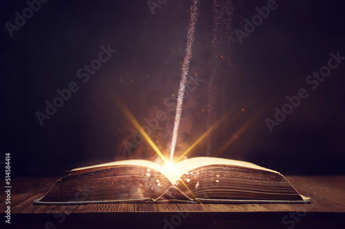 image of open antique book on wooden table with glitter overlay © tomertu