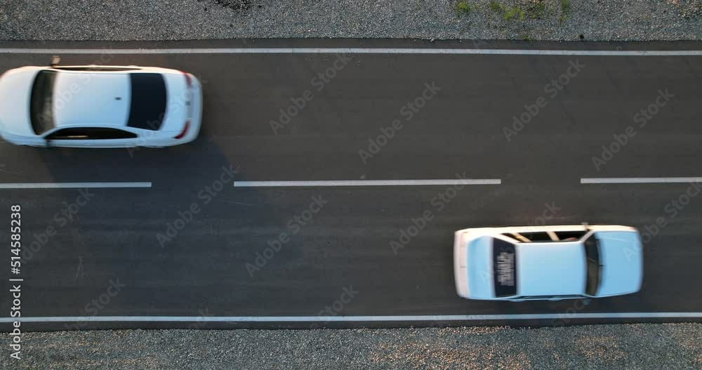 Two white cars drive along an asphalt road towards each other. Static video, Aerial view. The roadway from a height.