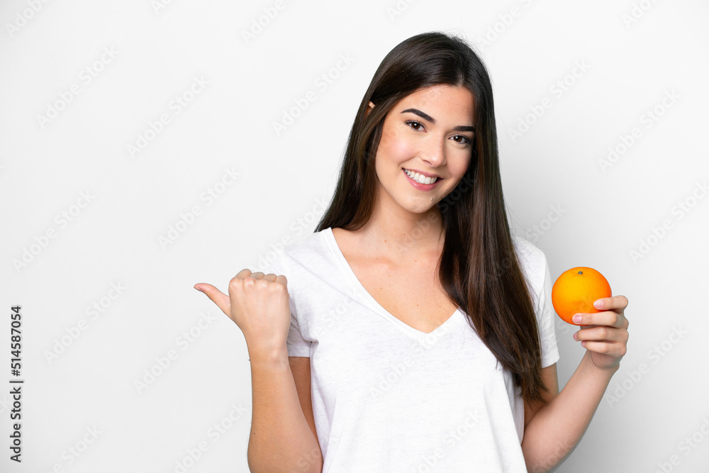 Young Brazilian woman holding an orange isolated on white background pointing to the side to present a product Young Brazilian woman holding an orange isolated on white background pointing to the side to present a product